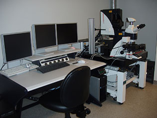 CLSM SP5 Image of a CLSM SP5 confocal microscope to the right of a desk with three white monitors on top