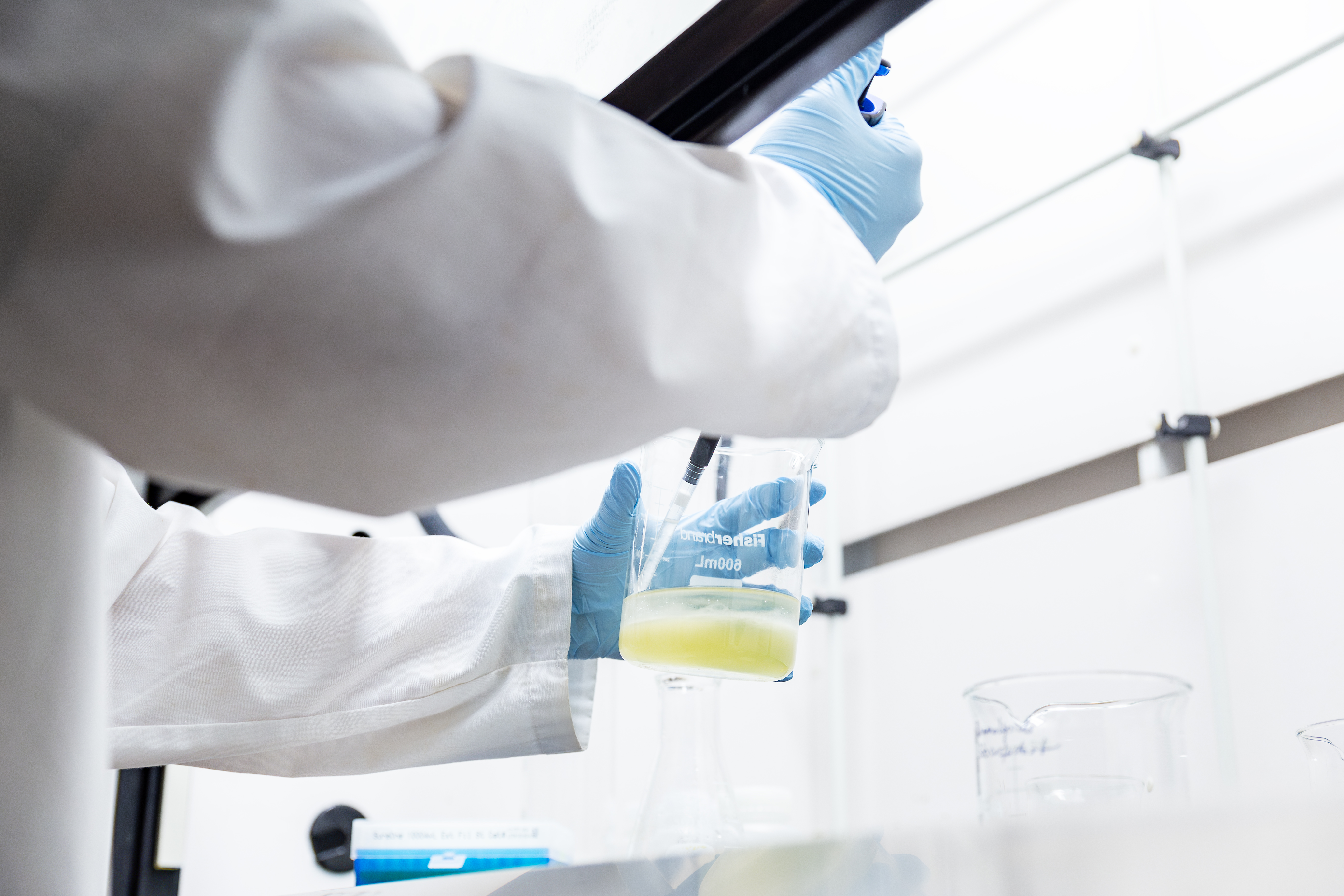 A person in a white lab coat with a syringe and a container with liquid in their hands